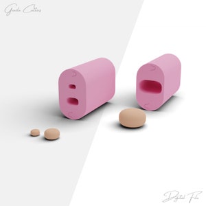 Puede incluir: Molde de plástico rosa con dos recortes redondos. El molde se muestra en dos vistas, una cerrada y otra abierta. La vista abierta muestra los recortes redondos. Hay tres pequeños objetos redondos de color beige junto al molde.