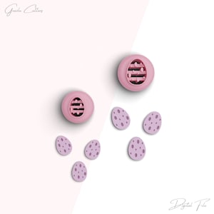 May include: Pink and purple plastic Easter egg cookie cutters. The larger cutters have a patterned design and the smaller cutters are solid.