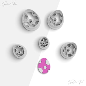 May include: Five white plastic cookie cutters shaped like eggs with different patterns. The cutters are arranged on a white surface. There is a pink egg with white polka dots in the center of the image.