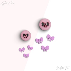 Op de afbeelding: Twee roze plastic koekjesvormen in de vorm van strikken, met vijf kleinere roze plastic strikvormen.