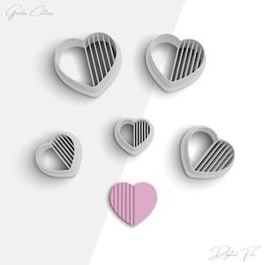 Könnte beinhalten: Fünf herzförmige Ausstecher mit einem gestreiften Design. Die Ausstecher sind aus weißem Kunststoff und auf einem weißen Hintergrund angeordnet. Ein Herz ist rosa und hat ein gestreiftes Design.