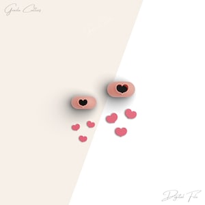 Könnte beinhalten: Zwei rosa Silikon-Ausstecher in Herzform mit schwarzen Herzen im Inneren. Es gibt auch mehrere rosa herzförmige Ausstecher, die um die Ausstecher herum verstreut sind.