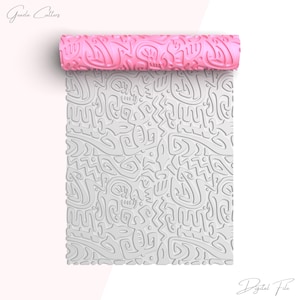 May include: A pink rolling pin with a white, abstract pattern. The pattern is a repeating design of geometric shapes and lines. The rolling pin is unrolled, showing the pattern on the surface.