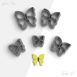 May include: Five gray plastic butterfly cookie cutters and one yellow butterfly cookie cutter. The cookie cutters are arranged on a white background.