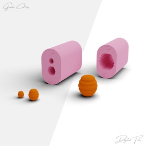 May include: Pink silicone mould with two round cavities for making honeycomb-shaped spheres. The mould is open to show the cavities. There are three orange honeycomb spheres of different sizes.
