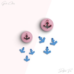 May include: A set of seven anchor-shaped cookie cutters. Two large cutters are pink and five smaller cutters are blue. The cutters are arranged on a white surface.