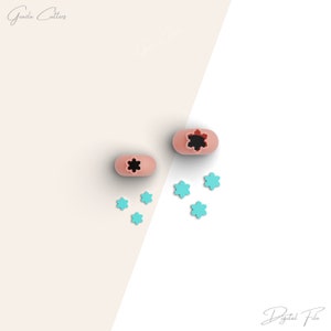 May include: Two pink silicone cookie cutters shaped like a flower with a black centre. There are six turquoise flower-shaped cookie cutters scattered around the pink cutters.