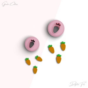 May include: Two pink plastic cookie cutters shaped like carrots. Five small orange and green plastic carrot shapes are scattered around the cutters.