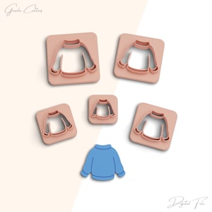 May include: Five cookie cutters in the shape of a sweater, in various sizes. The cutters are a light pink color. There is also a blue sweater in the center of the image.