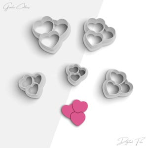 May include: Set of six heart-shaped cookie cutters, three with a single heart and three with three nested hearts. The cutters are white and are arranged on a white background. The image also includes a pink heart-shaped cookie cutter.