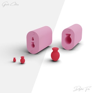 Op de afbeelding: Twee roze siliconen mallen voor het maken van kleine, ronde, vaasvormige objecten in rood. De mallen zijn aan één kant open en hebben een gedetailleerd ontwerp van een vaas met een rond lichaam en een smalle hals. Naast de mallen zijn drie rode vazen te zien.
