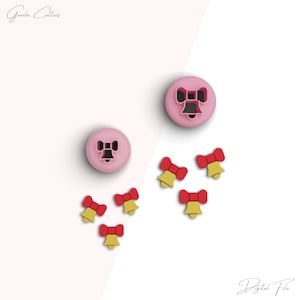 Puede incluir: Dos cortadores de galletas rosas en forma de lazos y cinco cortadores de galletas rojos y dorados en forma de campanas con lazos. Los cortadores de galletas están sobre un fondo blanco y rosa. Archivo digital.