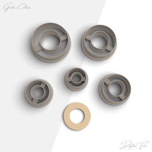 Puede incluir: Conjunto de seis cortadores de galletas de plástico gris de diferentes tamaños, con forma de anillo con un anillo más pequeño en el interior. Los cortadores están dispuestos sobre una superficie blanca. El texto "Archivo digital" es visible en la esquina inferior derecha.
