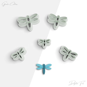 May include: Set of six dragonfly cookie cutters in a light blue colour. The cutters are arranged on a white background. The cutters are in various sizes and shapes.  The image also includes a single blue dragonfly cookie cutter.