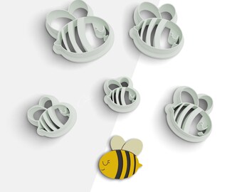 May include: Set of six bee-shaped cookie cutters. The cutters are white and come in different sizes. The smallest cutter is a cartoon bee with yellow and black stripes. The other cutters are more stylized and have a simple design.