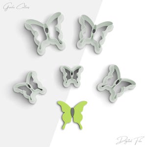May include: Set of six white plastic butterfly cookie cutters, with a green butterfly cookie cutter in the center.