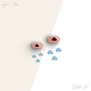 Puede incluir: Dos moldes de silicona rosa con un recorte en forma de nube. Los moldes están rodeados de pequeñas formas de nubes de silicona azul.