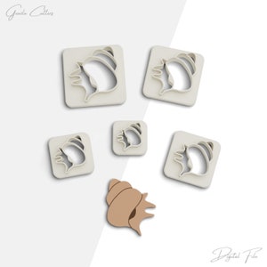 Op de afbeelding: Vijf witte plastic koekjesvormen in de vorm van schelpen. De vormen zijn gerangschikt op een witte achtergrond. Een bruine schelp bevindt zich in het midden van de afbeelding.