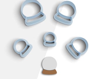 May include: Set of six blue plastic cookie cutters shaped like snow globes. The cutters are arranged on a white background. The largest cutter is in the center of the image. The smallest cutter is in the lower left corner of the image. The cutters are all different sizes.