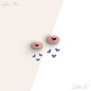 以下が含まれることがあります： コウモリの切り抜きが付いた2つのピンク色の楕円形のクッキーカッターと、いくつかの小さな紫色のコウモリ型の切り抜き。 画像は対角線で分割された背景で、左側に薄いベージュ、右側に白があります。