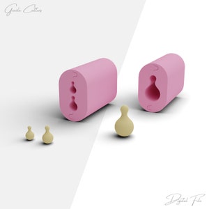 May include: Pink silicone mold with two cavities shaped like a pear. The mold is open and there are three small pear-shaped objects made of a light yellow material.
