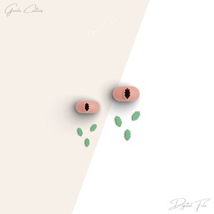 Puede incluir: Dos cortadores de galletas de silicona rosa en forma de hojas de roble. Los cortadores están sobre una superficie blanca con cinco cortadores de hojas de silicona verde esparcidos a su alrededor.