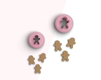 May include: A set of gingerbread man cookie cutters. The set includes two pink plastic cutters, one large and one small, and five brown gingerbread men cookies.