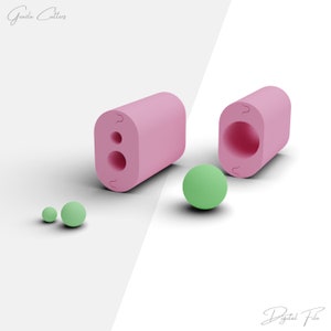 May include: Pink silicone mold with two round cavities for making small round candies or chocolates. The mold is open to show the inside of the cavities. There are three green spheres next to the mold.