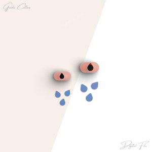 May include: Two pink silicone cookie cutters shaped like raindrops with black centres. Five blue silicone cookie cutters shaped like raindrops are scattered below.