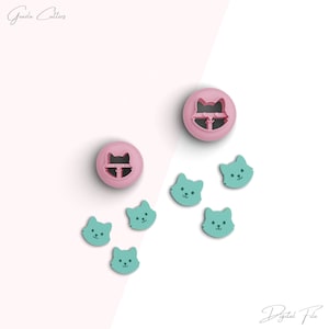 May include: A set of six cat-shaped cookie cutters. Two of the cutters are pink and feature a cat face with a closed mouth. The other four cutters are teal and feature a cat face with an open mouth.