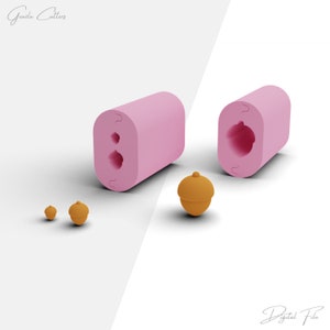 May include: A pink silicone mold with two acorn-shaped cavities. The mold is shown next to three brown acorn-shaped objects. The text "Gazda Cutters" is visible in the top left corner of the image.