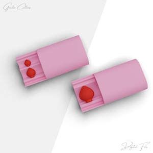 May include: Two pink silicone molds for making heart-shaped treats. The molds are open to show the heart-shaped cavities inside. The molds are on a white background.