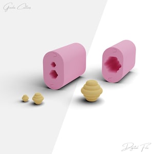 May include: Pink silicone mold with two round cavities for making small, round, layered pastries. The mold is open and shows the inside of the cavities. There are three small, round, layered pastries in the image, one of which is in the mold.