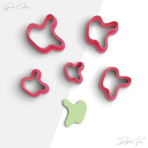 May include: Set of six pink cookie cutters in various abstract shapes. The cutters are arranged on a white background.  The cutters are designed to create unique and modern cookies.