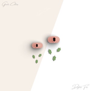 May include: Two pink silicone cookie cutters shaped like stars with a holly leaf design. The cutters are on a white background with green holly leaves scattered around them.