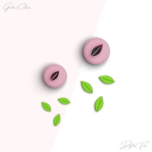 Puede incluir: Dos cortadores de galletas de color rosa en forma de melocotón con un corte en forma de hoja en el centro. Cinco cortadores de galletas de hoja verde están dispersos alrededor de los melocotones.