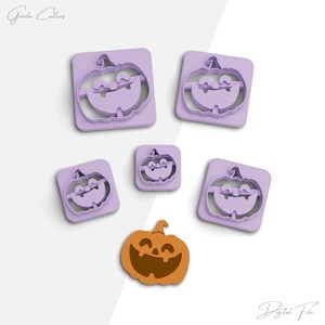 Puede incluir: Cinco cortadores de galletas de calabaza de plástico morado de diferentes tamaños, con una sola galleta de calabaza naranja sobre un fondo blanco. Los cortadores de galletas tienen una cara de calabaza sonriente.