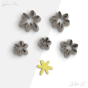 Könnte beinhalten: Satz von sechs grauen, blumenförmigen Ausstechern, mit einem gelben, blumenförmigen Ausstecher in der Mitte. Die Ausstecher sind in einem Kreis um den gelben Ausstecher angeordnet.