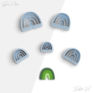 Puede incluir: Conjunto de seis cortadores de galletas con forma de arcoíris, cinco son de color azul claro y uno es verde. Los cortadores tienen la forma de un arcoíris con arcos de diferentes tamaños.