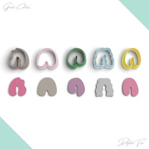 Puede incluir: Conjunto de diez cortadores de galletas en varios colores y formas, incluyendo una forma ondulada, una forma redondeada y una forma de corazón. Los cortadores están dispuestos en dos filas sobre un fondo blanco.