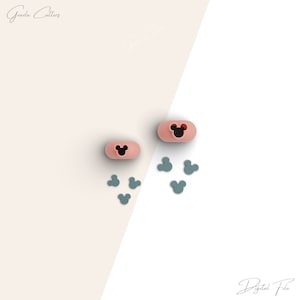 以下が含まれることがあります： 黒い耳が付いたミッキーマウスの頭の形をしたピンクのシリコン製クッキーカッターが2つ。大きなカッターの周りに、小さな青いシリコン製ミッキーマウスの頭の形をしたクッキーカッターが6つ散らばっています。