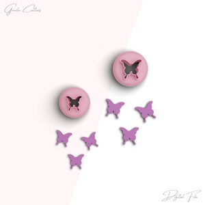 May include: A set of pink butterfly cookie cutters. The set includes two large cutters and five smaller cutters. The cutters are arranged on a white and pink background.