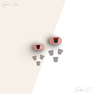 May include: Two pink plastic cookie cutters shaped like flower pots, with five smaller gray plastic cookie cutters shaped like flower pots.