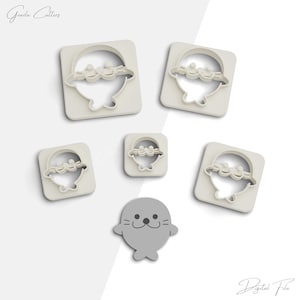 May include: Set of five cookie cutters in the shape of a seal. The cutters are white and come in different sizes. The largest cutter is a square with a seal inside. The other cutters are round and feature a seal with its flippers up. The smallest cutter is a single seal with its flippers down.