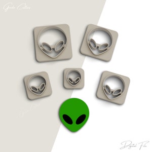 May include: Set of six cookie cutters in the shape of an alien head. The cutters are made of a light gray plastic and are arranged on a white background. The cutters are in various sizes. A green alien head cookie is also shown.