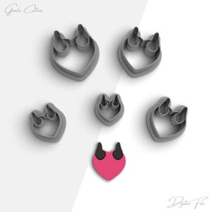 May include: A set of six grey cookie cutters shaped like hearts with horns. The cutters are arranged on a white background. There is a smaller red heart with horns in the center of the image.