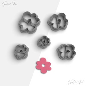 Puede incluir: Conjunto de seis cortadores de galletas de flores de plástico gris, con un cortador de galletas de flores rosa en el centro. Los cortadores de galletas tienen la forma de una flor simple de cinco pétalos.