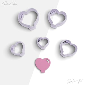 Op de afbeelding: Set van zes hartvormige koekjesuitstekers, vijf zijn lichtpaars en één is roze. De uitstekers hebben de vorm van een hart met een kleine ballonstaart.