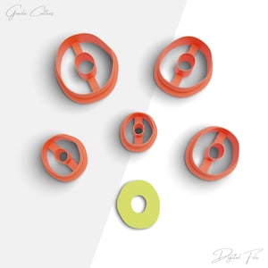 Puede incluir: Conjunto de seis cortadores de galletas de plástico naranja en varios tamaños y formas, incluyendo círculos y óvalos, con un solo cortador de rosquilla de plástico verde.