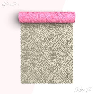 Puede incluir: Se muestra un rodillo rosa con un diseño de hojas, junto con una lámina de masa con el mismo diseño. El rodillo es de un rosa vibrante, y el diseño de hojas es visible tanto en el rodillo como en la masa.